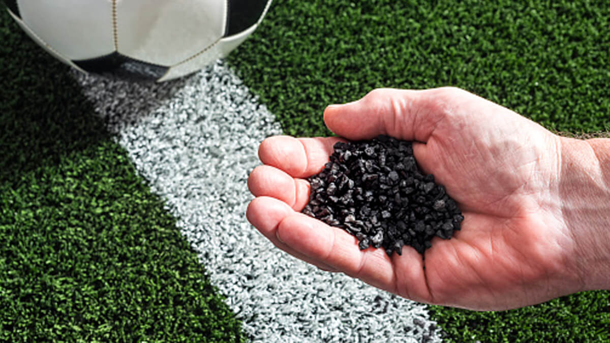 A hand holding rubber turf pellets over a soccer field