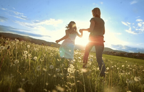 A woman and child running hand in hand through a field