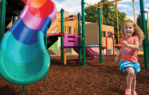 A little girl running through a playground filled with rubber mulch