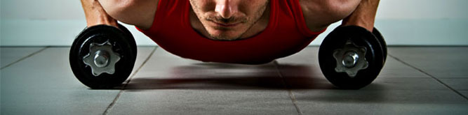 A man doing weighted dumbbell push ups on rubberized floor
