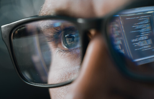 A close up on glasses as someone stares at a computer monitor