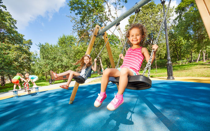 Girls swinging on a playground with recycled rubber turf